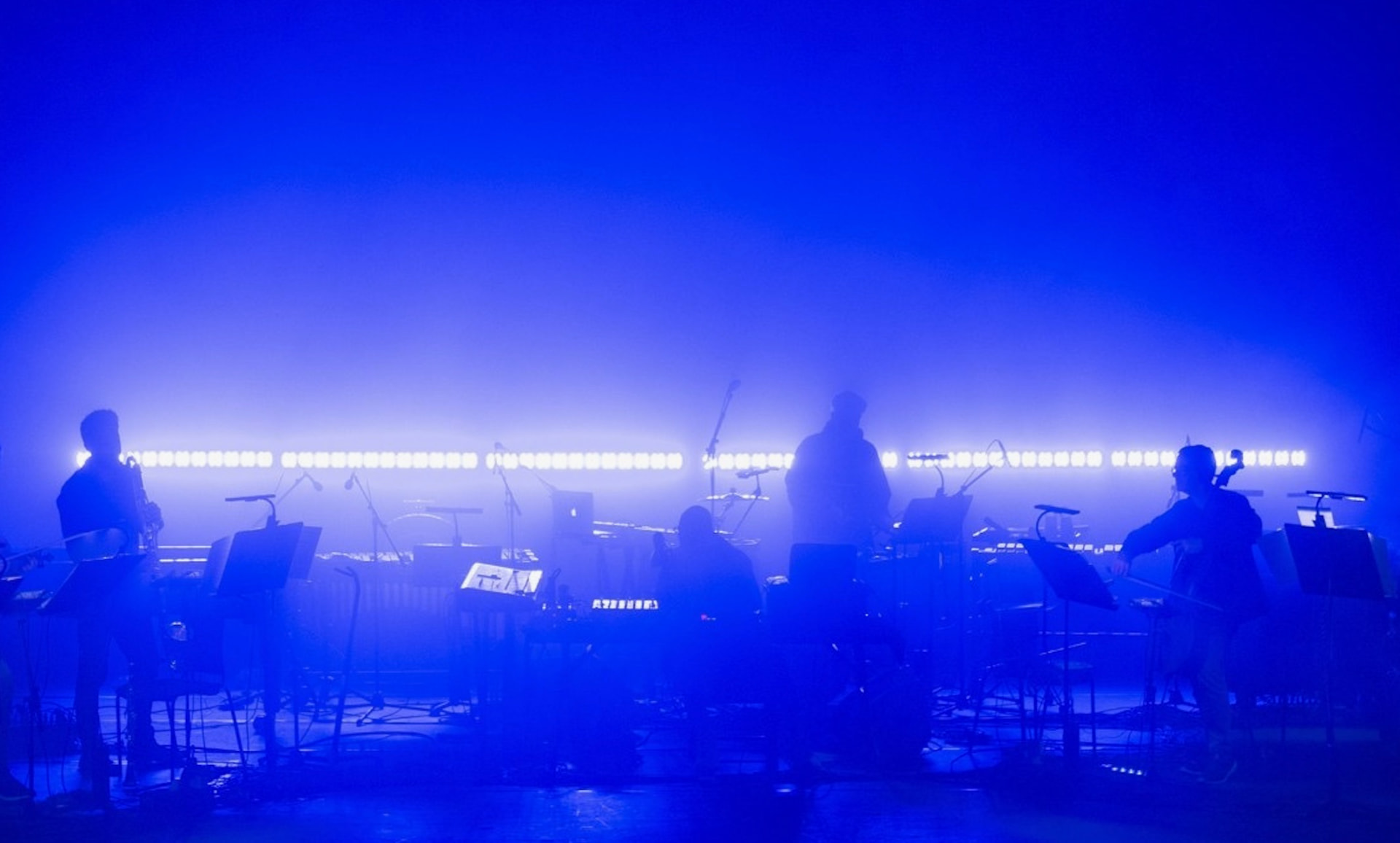 Ensemble silhouetted against a wall of blue light and haze