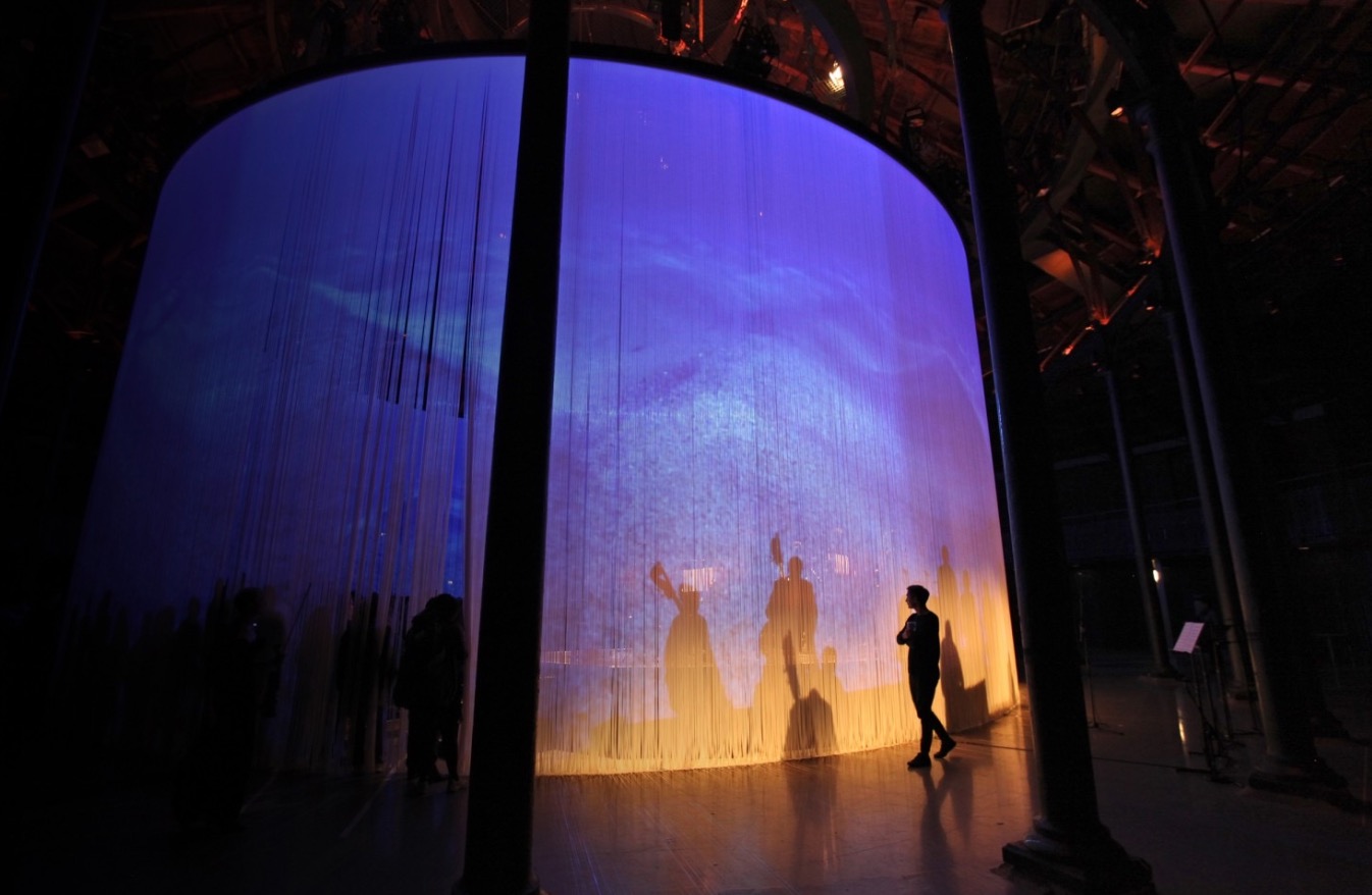 Audience walking around a curved projection installation lit violet and gold